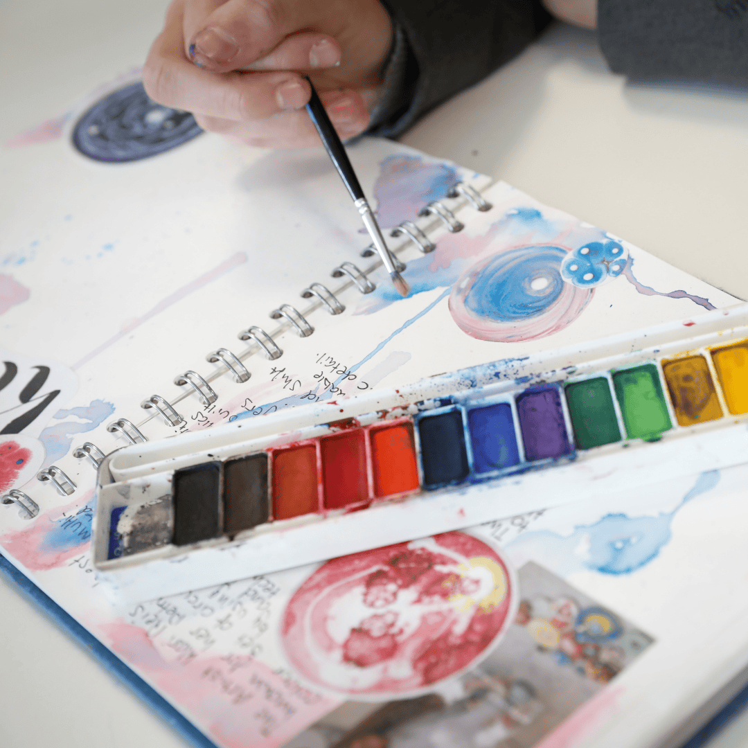 A student paints in their art sketchbook at Laurus Cheadle Hulme