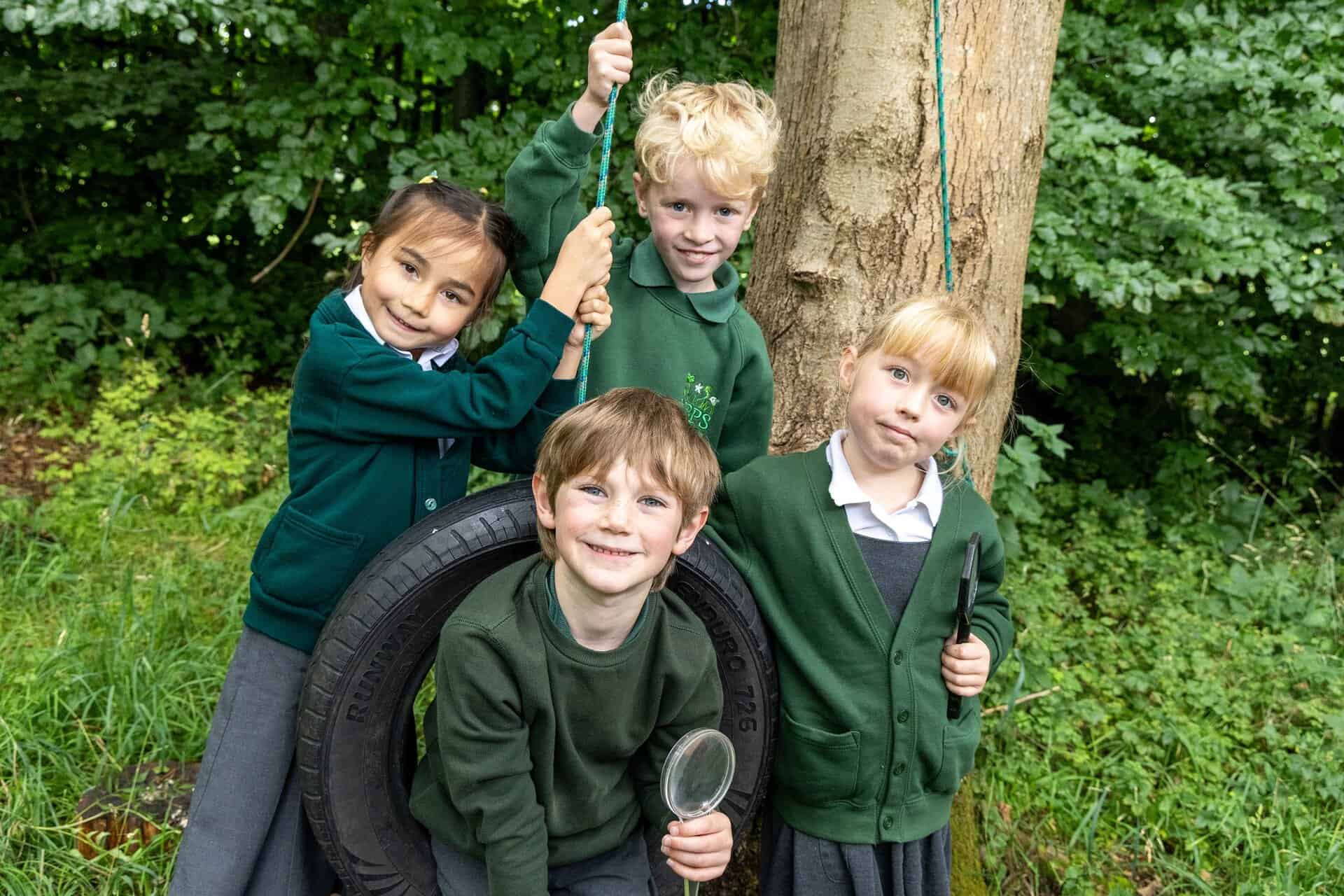 Pupils smile and gather around a tyre swing in the forest school area at Norris Bank Primary School